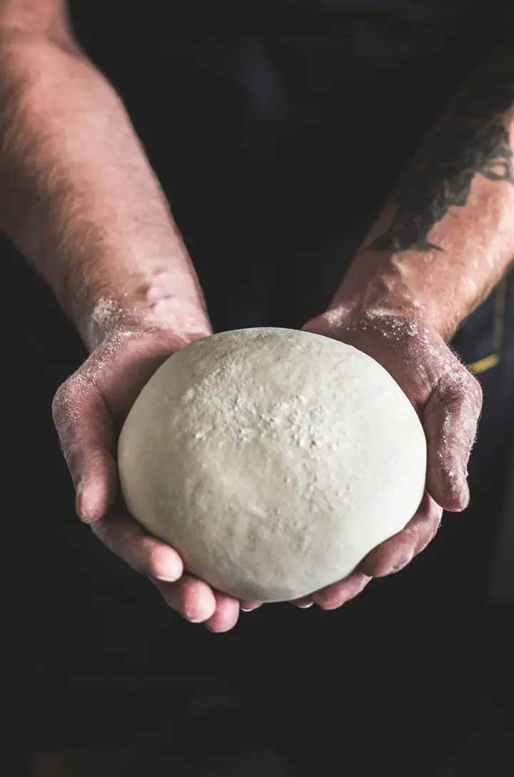 Hands stretching Neapolitan pizza dough on a floured wood surface