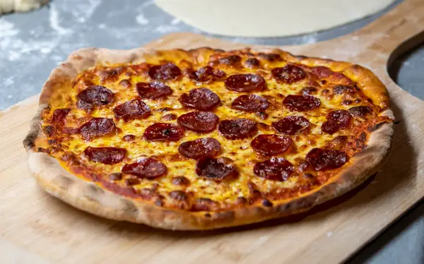 A pepperoni pizza on a wooden tray with cup-and-char pepperoni edges curled up into bowls