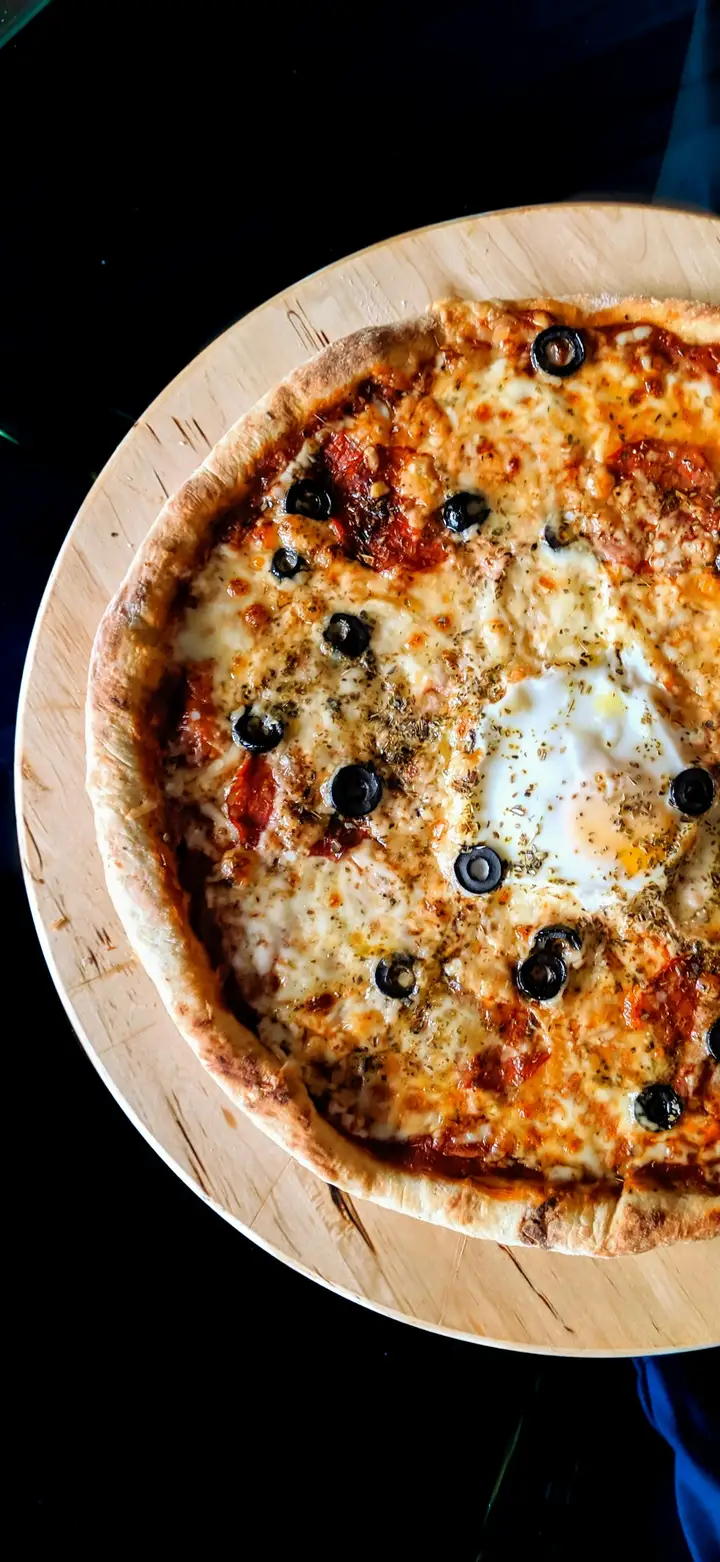 Wood fired pizza oven with flames visible in the chamber and a pizza cooking on the stone surface