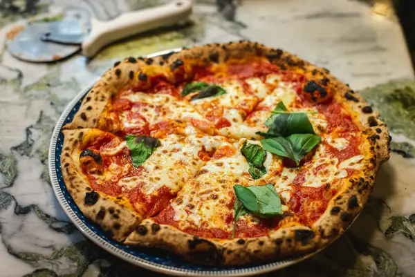 Pizza baking in a high-temperature oven with flames visible, showing the heat range needed for Neapolitan style pizza