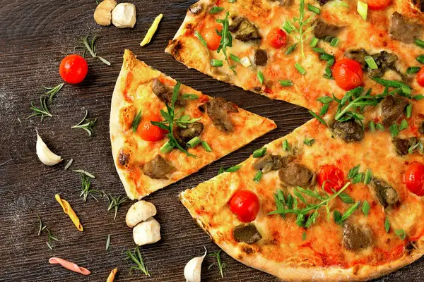 A thin, crispy tavern style pizza topped to the edge with vegetables and herbs, on a dark wooden board