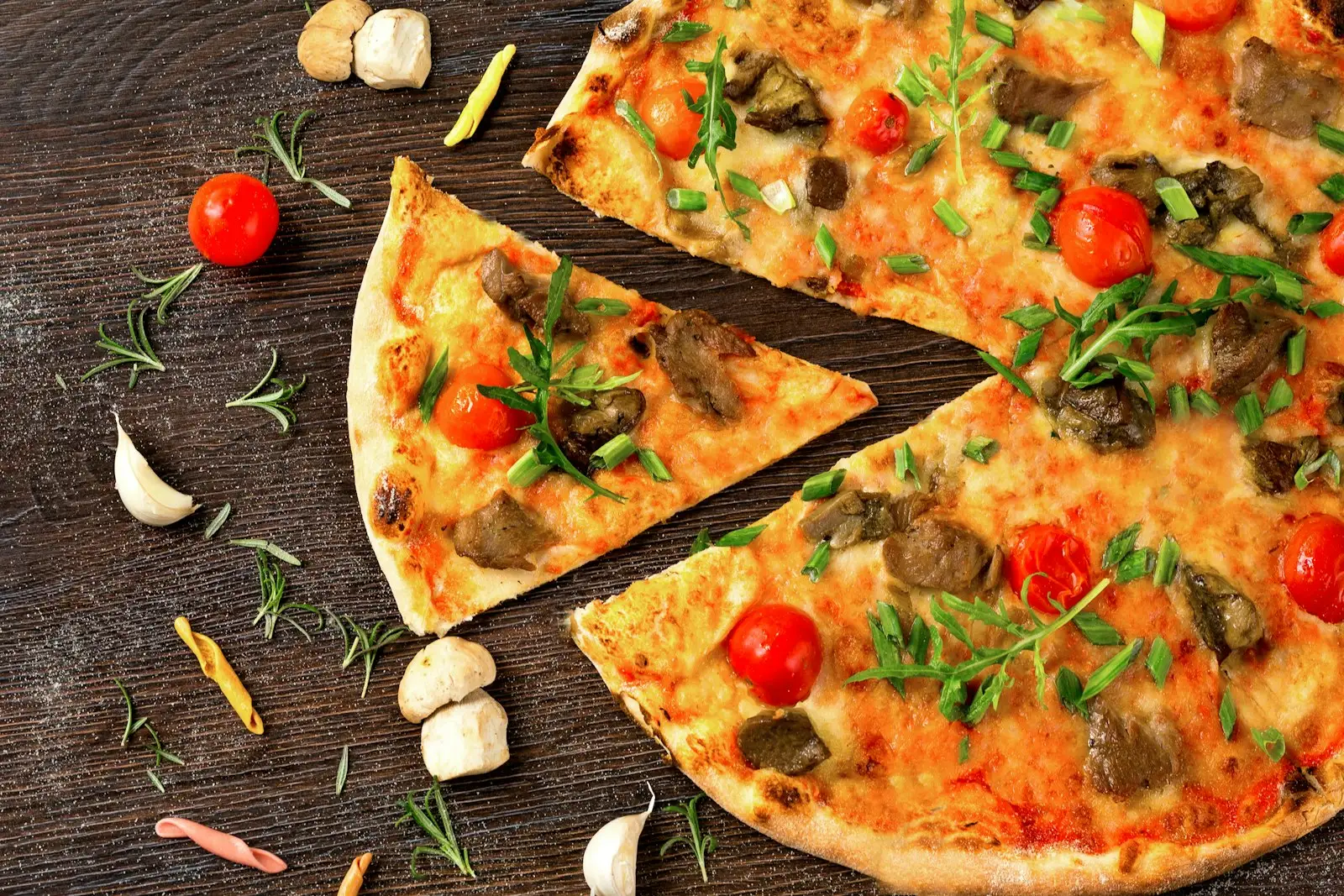 A thin, crispy tavern style pizza topped to the edge with vegetables and herbs, on a dark wooden board