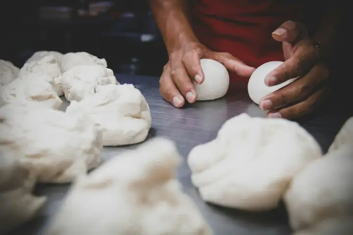 Hands rounding pizza dough into balls on a steel counter, the step after a bread machine pizza dough cycle