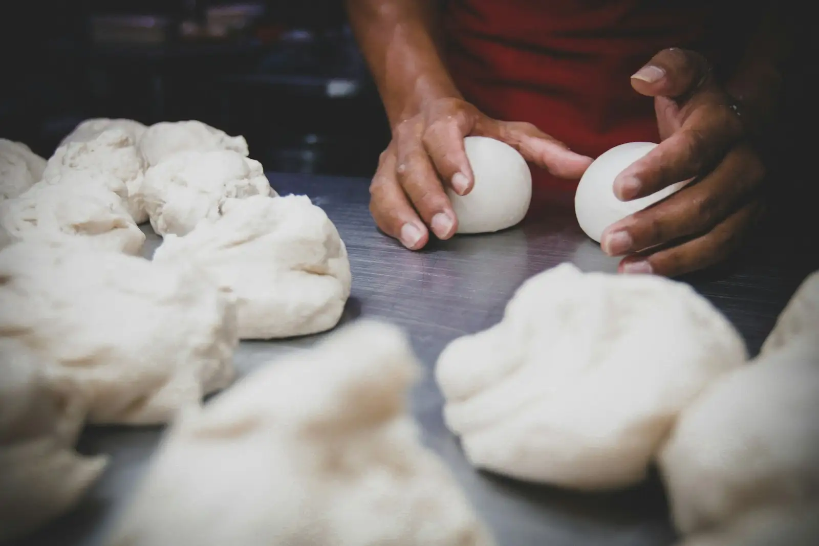 Hands rounding pizza dough into balls on a steel counter, the step after a bread machine pizza dough cycle