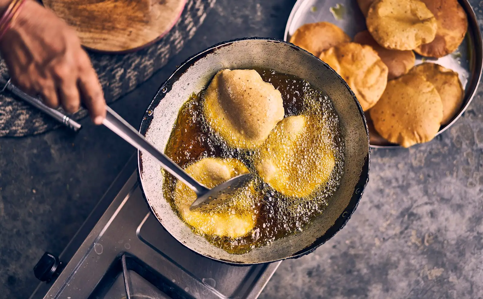Dough rounds puffing in a pan of hot oil while a cook bastes them, the same fry-and-baste method used for panzerotti