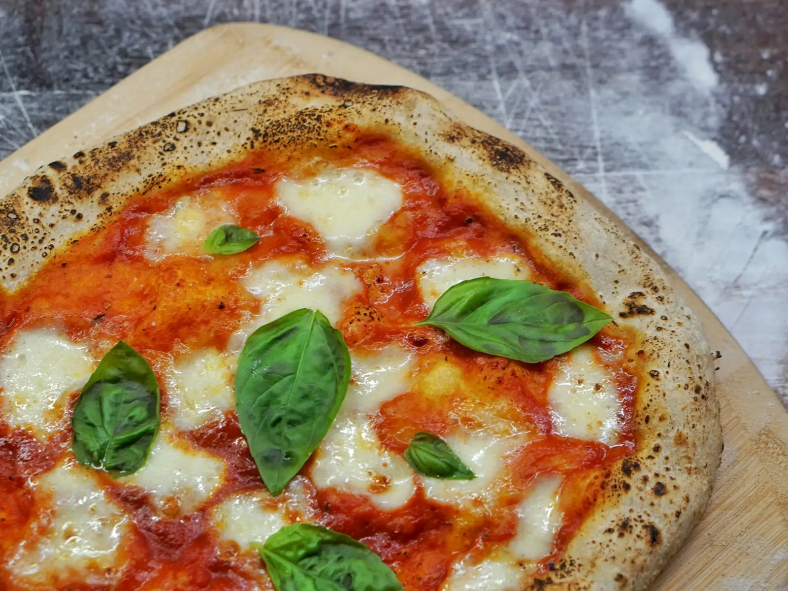 Sourdough pizza dough with an open, airy crumb and blistered fermented crust on a wooden surface