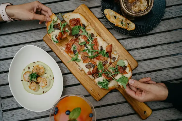 An oblong pinsa-style flatbread topped after baking with prosciutto, arugula, and figs, sliced on a wooden board