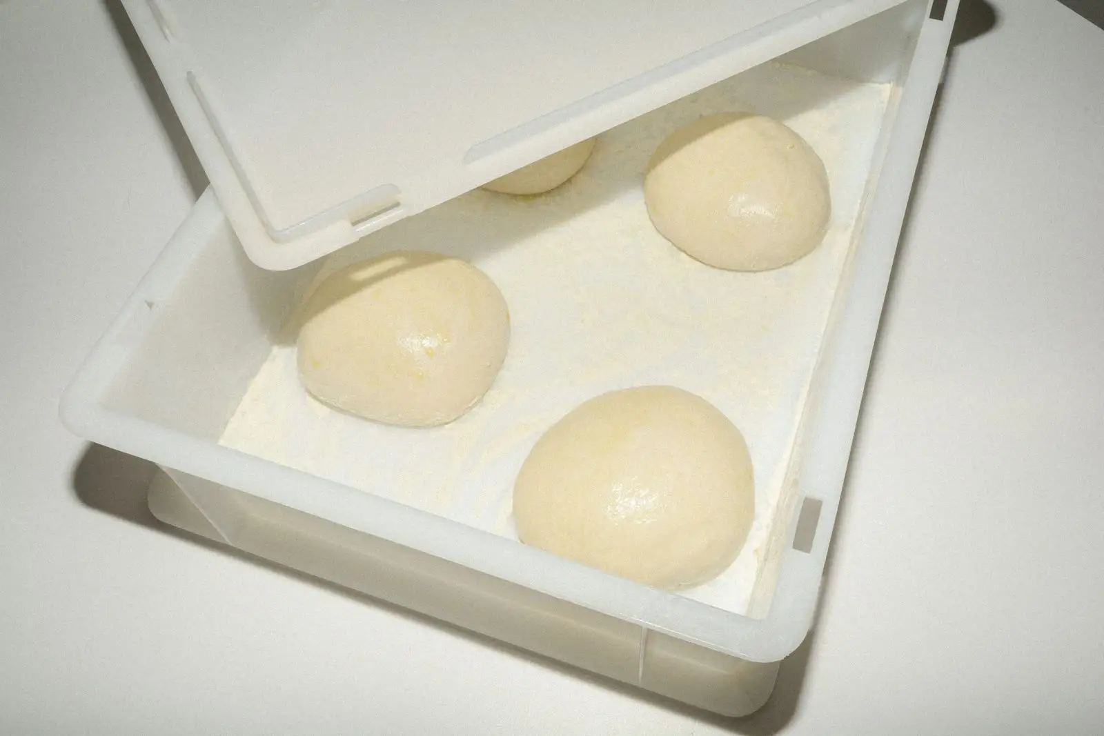 Four smooth balls of proofed pizza dough resting in a flour-dusted proofing box