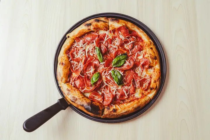 A Sicilian-style pan pizza on a tabletop, the rectangular pan format with golden cheese and crisp olive-oiled bottom