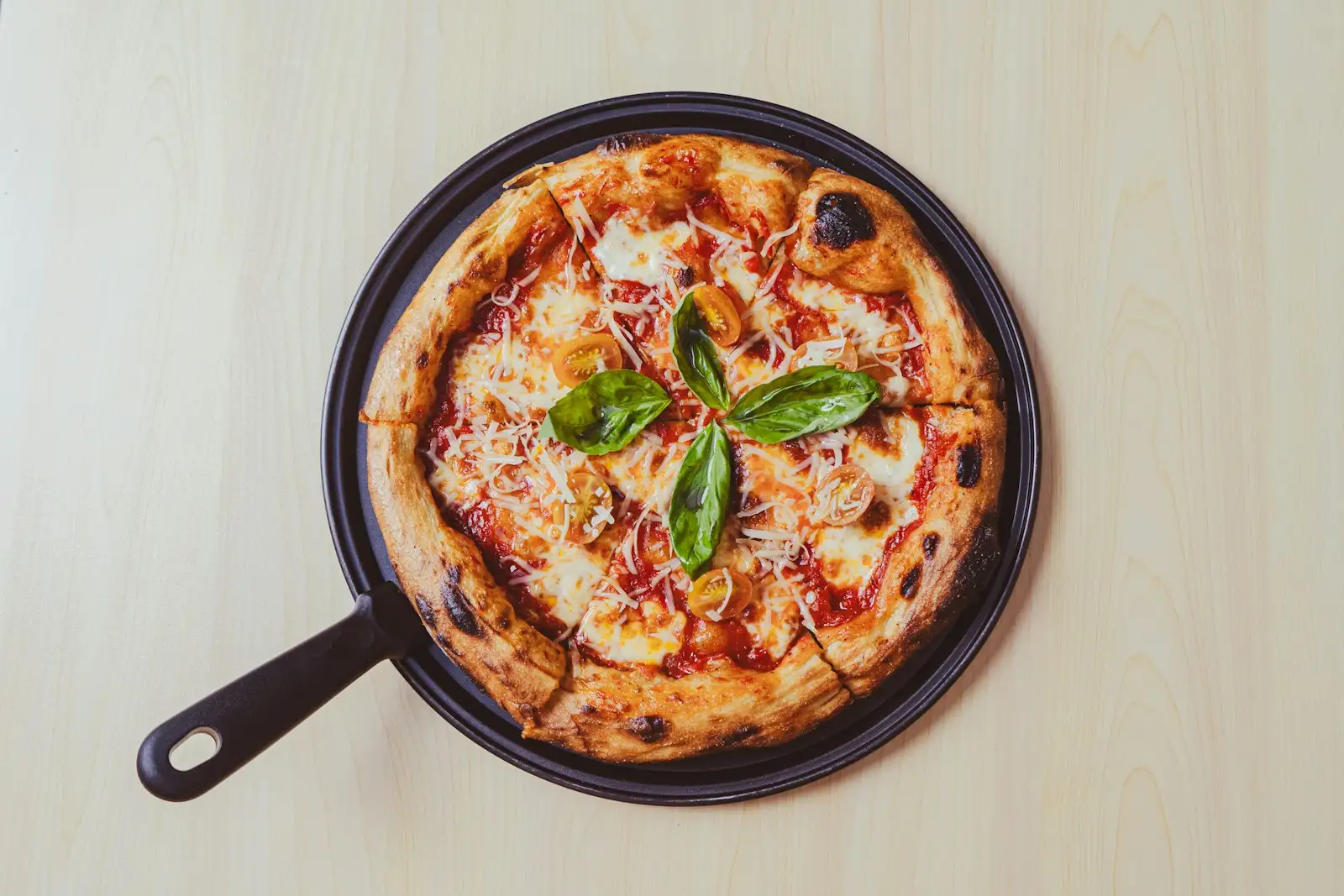 Cast iron skillet pizza with a puffed, charred crust, melted mozzarella, cherry tomatoes, and basil, baked in a dark pan