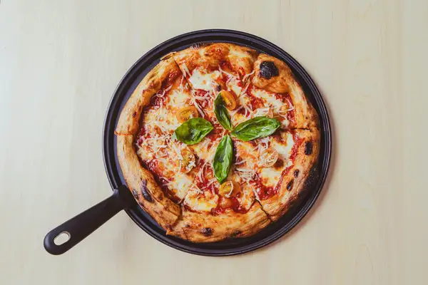 Cast iron skillet pizza with a puffed, charred crust, melted mozzarella, cherry tomatoes, and basil, baked in a dark pan