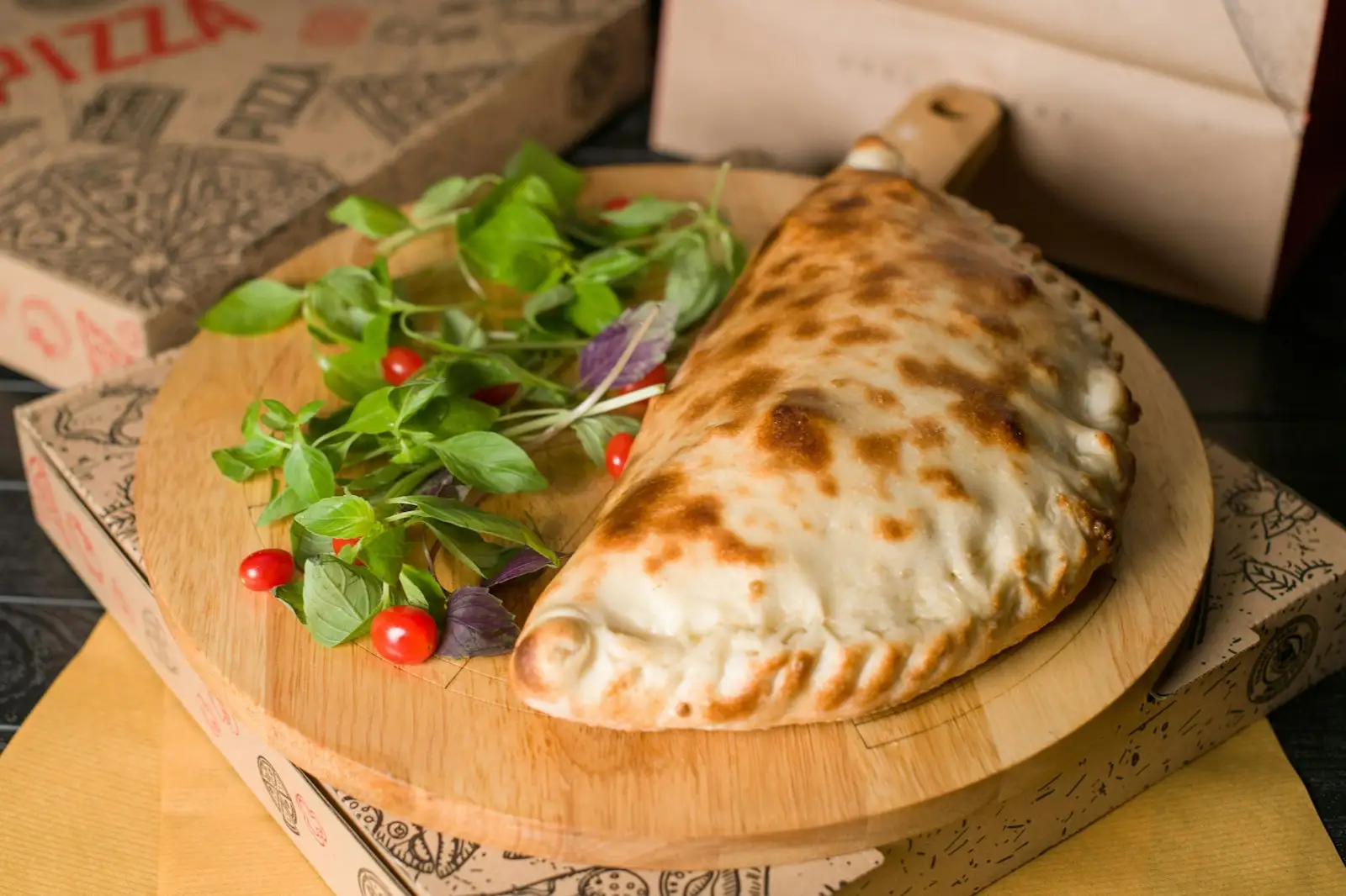 A golden, folded half-moon calzone on a wooden board, the sealed crimped edge that sets a calzone apart from a stromboli
