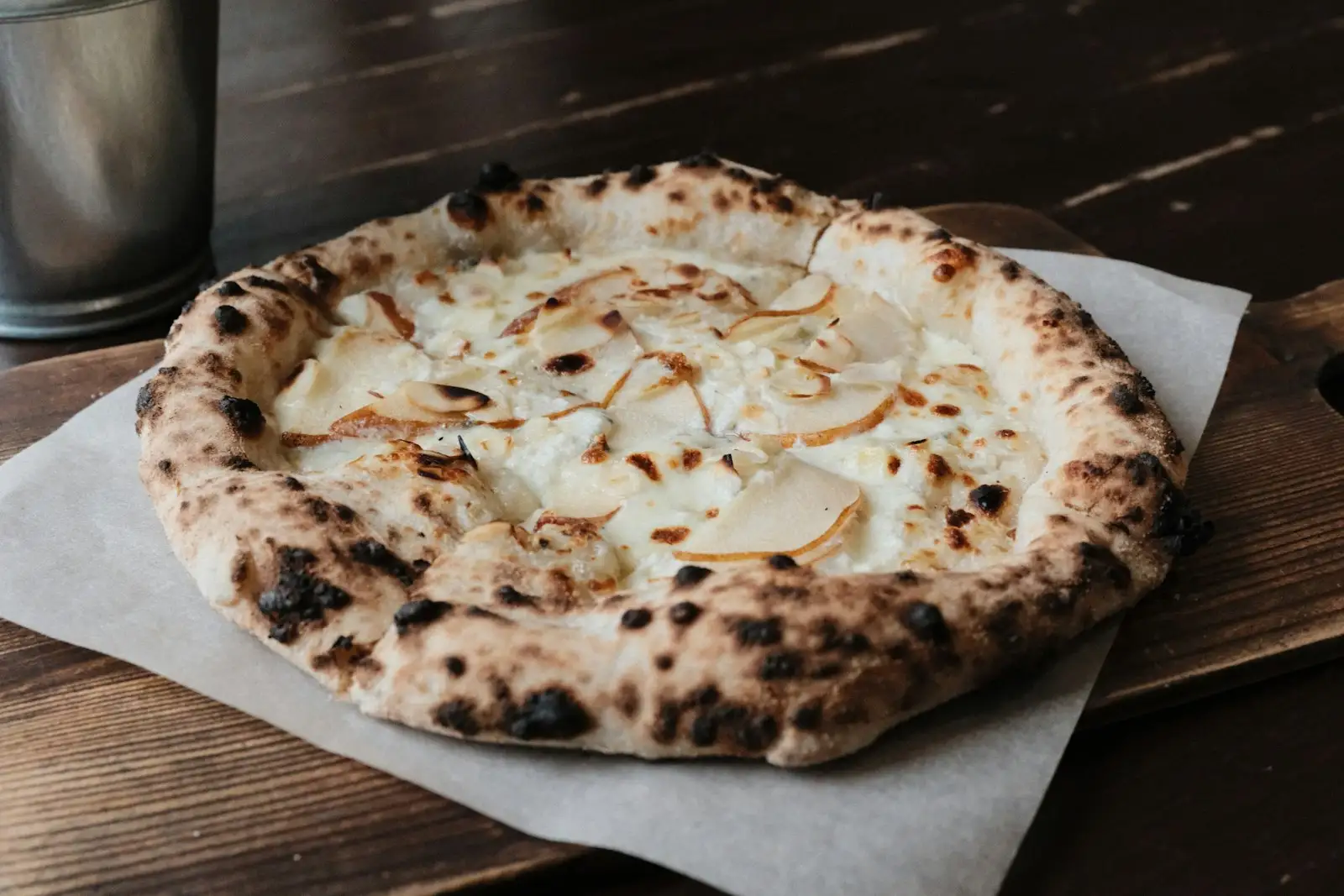 A rustic pear and cheese white pizza on a wooden board, the kind of pie that uses white sauce or olive oil instead of red tomato sauce