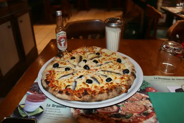 A whole anchovy pizza topped with a radial pattern of anchovy fillets and black olives on a white plate